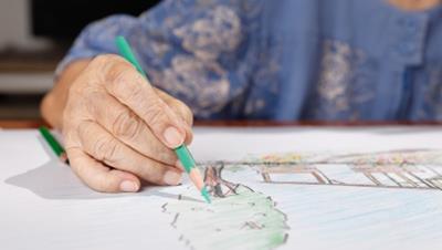 An older person drawing with a turquoise colored pencil