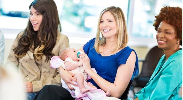 Beautiful mid adult Caucasian working mom holds her infant daughter during a discussion group with her peers. She is dressed in business attire.