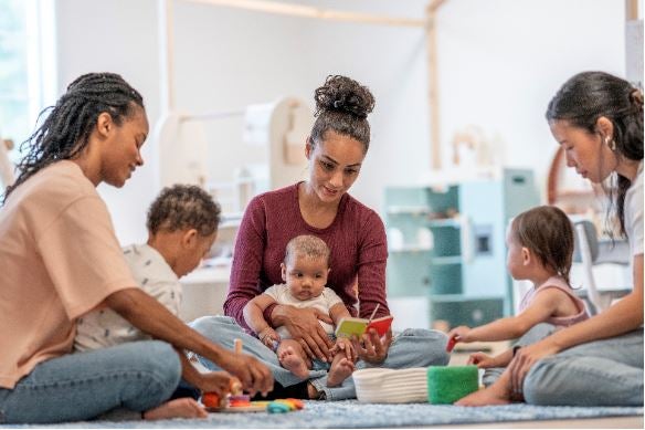A diverse group of mothers and children enjoy learning and bonding in a bright, child-friendly environment filled with educational toys promoting development and connection.